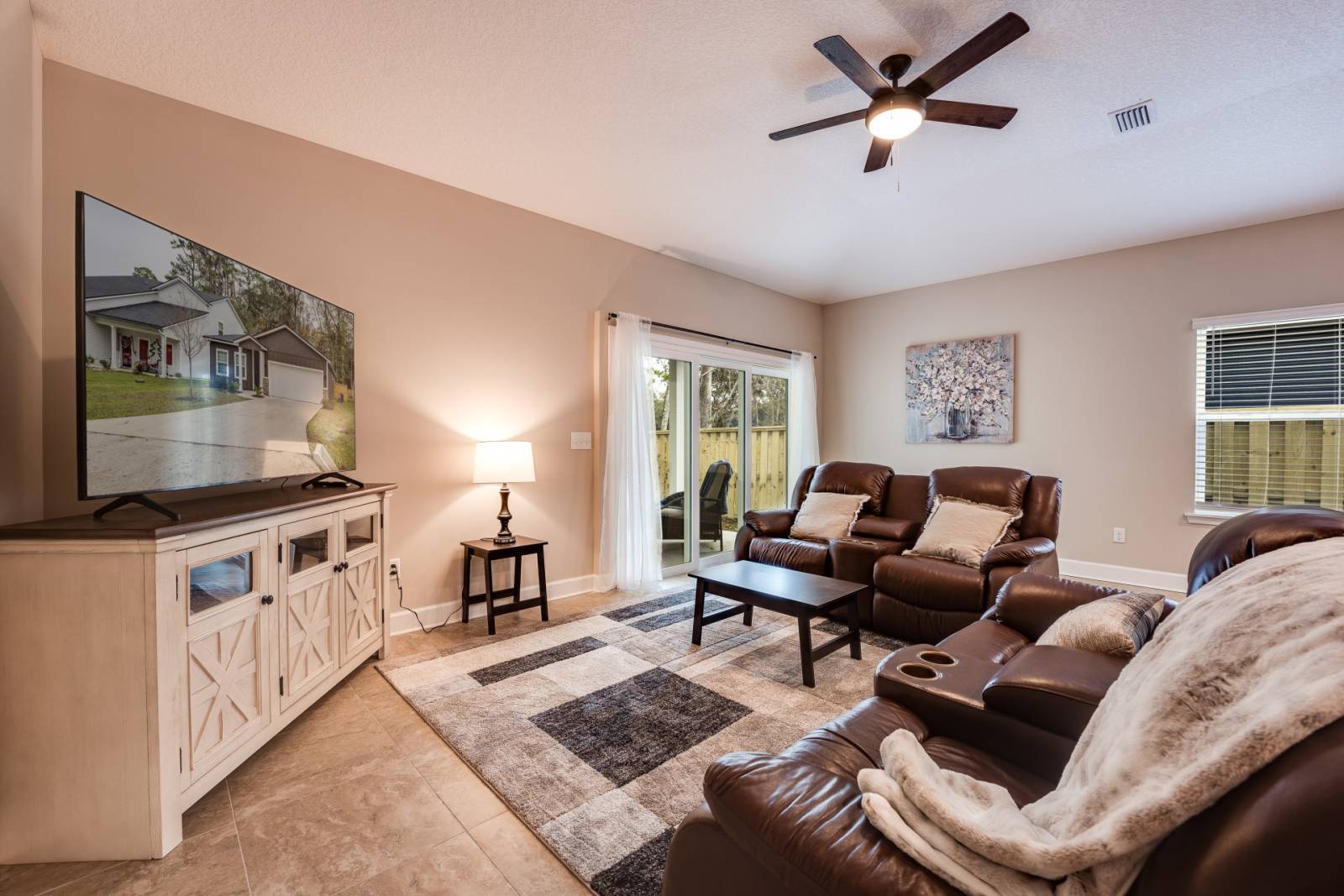 Living room with chairs, coffee table, pair of chairs, large tv, lamp, sliding glass doors that lead to backyard.
