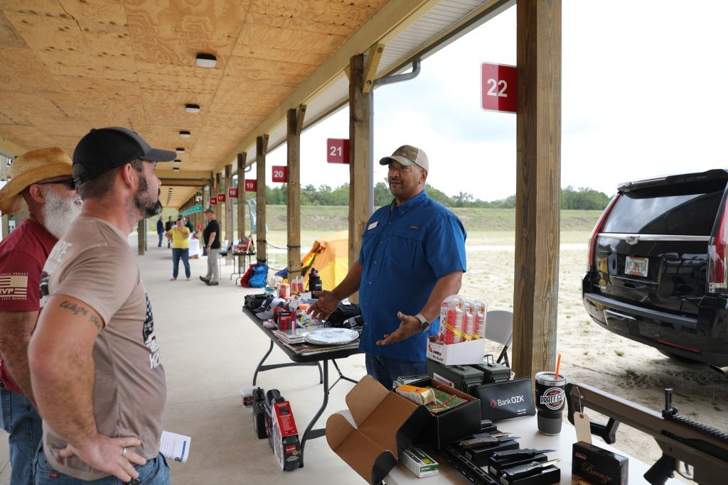a man in a blue shirt talking to two other males at a gun range