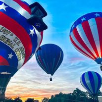 Hot air balloons in the air as the sun sets in the background.