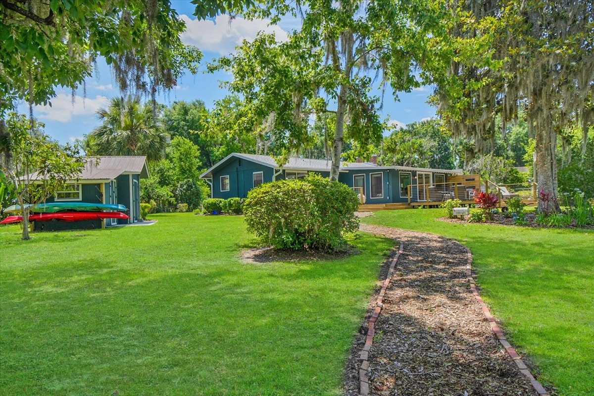 Blue house with a blue shed and a brick paved path leading through a green yard with kayaks mounted to the side