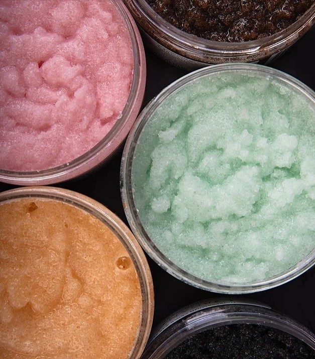 Brown sugar scrub in clear container, pink sugar scrub in clear container, light green sugar scrub in clear container, orange sugar scrub in clear container, black sugar scrub in clear container