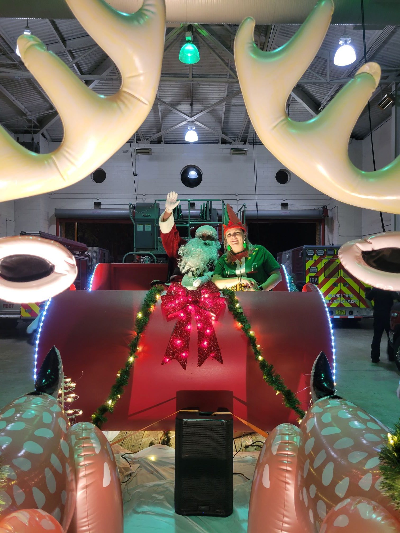 Santa and Mrs. Claus sitting in a sled at a fire station.