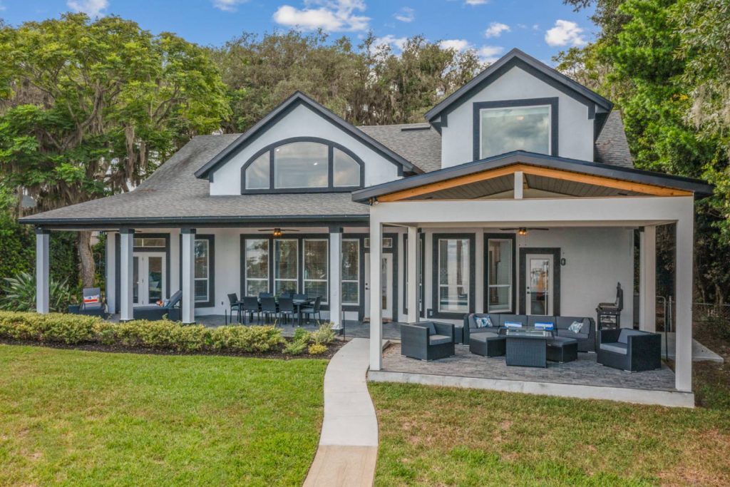 Large house with a wrap around back porch with lots of seating and a paved sidewalk