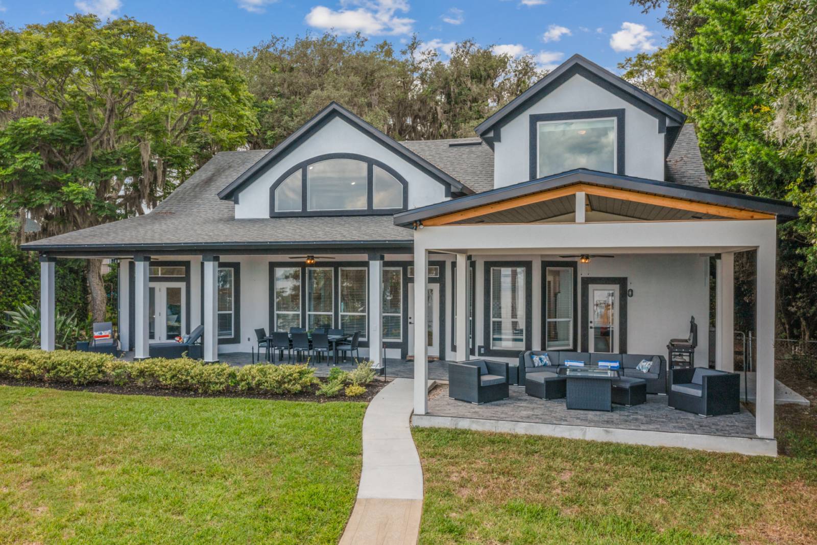 Large house with a wrap around back porch with lots of seating and a paved sidewalk