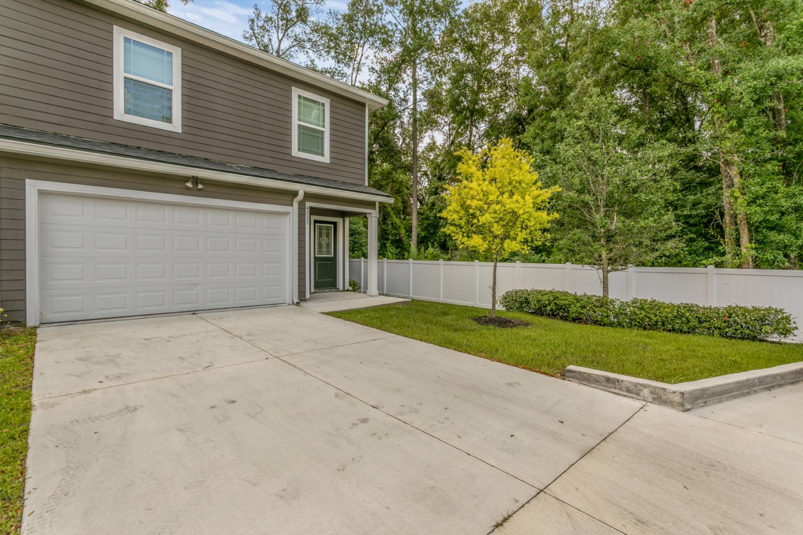 Neutral color townhome with a paved drive way and trees to the right of the property.