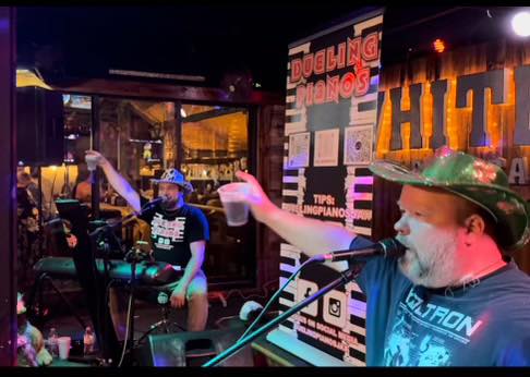 Image of two men at keyboard pianos and singing in a restaurant