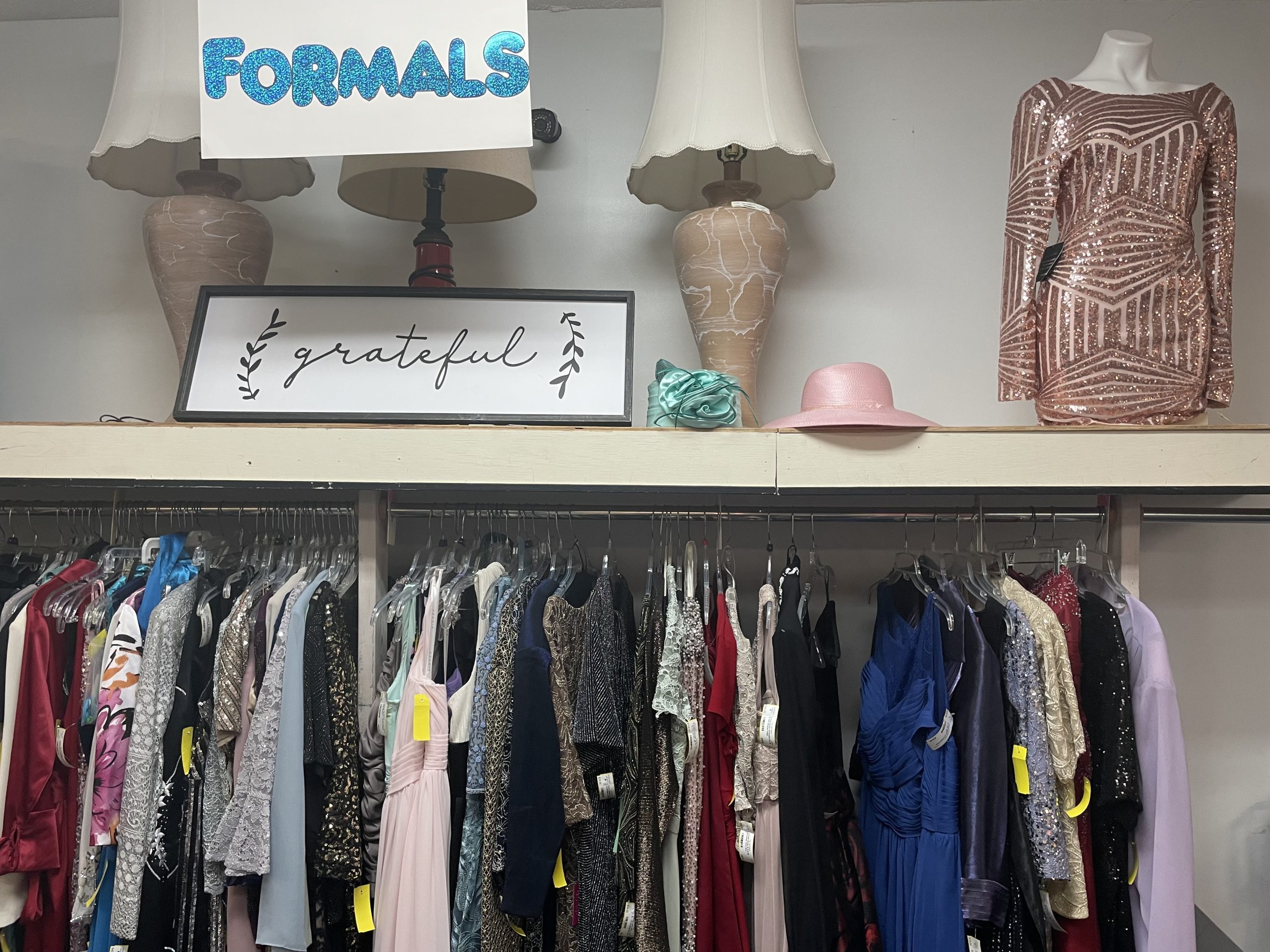 rack of clothing with lamps on a shelf at a thrift store